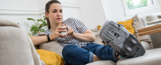 ILLUSTRATION - Eine Frau sitzt am 18.08.2020 in Wittenberge mit einem Gehgips am Fuss auf einer Couch (gestellte Szene)