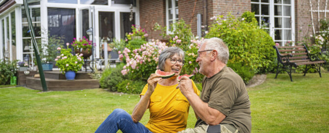 ILLUSTRATION - Ein aelteres Paerchen sitzt am 18.07.2023 in einem Garten in Uelsby auf dem Rasen und isst Melone (gestellte Szene)